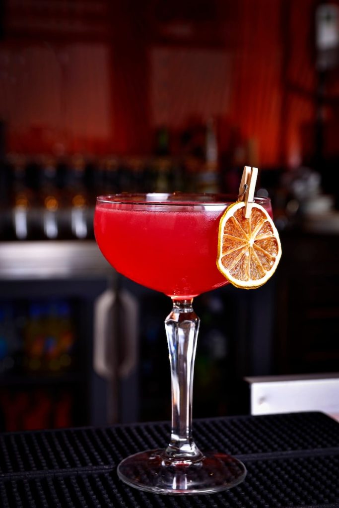 a red drink with a slice of lemon on the rim